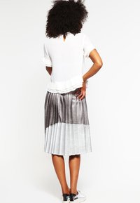 Bílý krátký rukáv top s volánkovým lemem a V-zadním výstřihem, spárovaný s plisovanou sukni ve stříbrné a šedé barvě, nošený se stříbrnými teniskami.