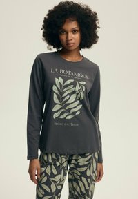 Szara bluzka z długim rękawem z zielonym nadrukiem liści i tekstem, zestawiona z dopasowanymi spodniami w tym samym wzorze, wykonana z miękkiego materiału.