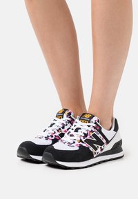 Baskets noir et blanc avec un motif floral coloré, présentant un design en suède et mesh, bout rond et semelle extérieure en caoutchouc.