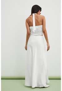 Ensemble en satin blanc à deux pièces comprenant un crop top à col halter avec un lien à l'arrière et une longue jupe fluide. Texture lisse et design épuré.