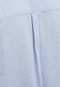 Tejido texturizado en azul claro con un brillo sutil. Presenta un pliegue en la espalda y líneas suaves y limpias, apto para vestimenta casual o formal.