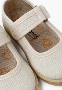 Pantofi Mary Jane din țesătură bej, cu o curea tip hook-and-loop, vârf rotund, suprafață texturată și talpă din fibră naturală cu cusături vizibile.