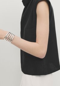 Black linen sleeveless top with a high neckline; silver twist bangle bracelet on arm; smooth texture, minimalist design.