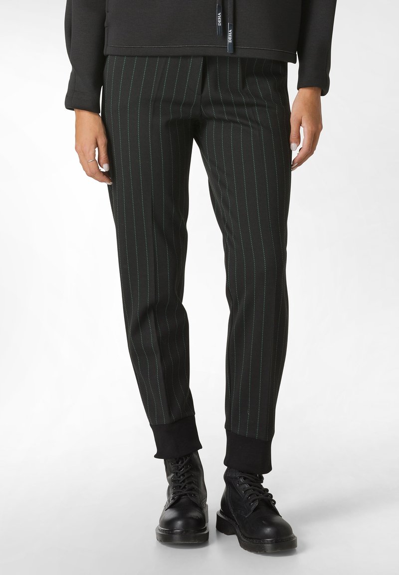 Pantalones negros de rayas con rayas verdes, de corte ajustado, con puños elásticos y bolsillos, combinados con botas negras con cordones.