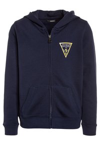 Hoodie zippé marine en mélange de coton. Il présente un logo triangulaire jaune "GUESS" sur la poitrine gauche et des poches kangourou. Texture douce.