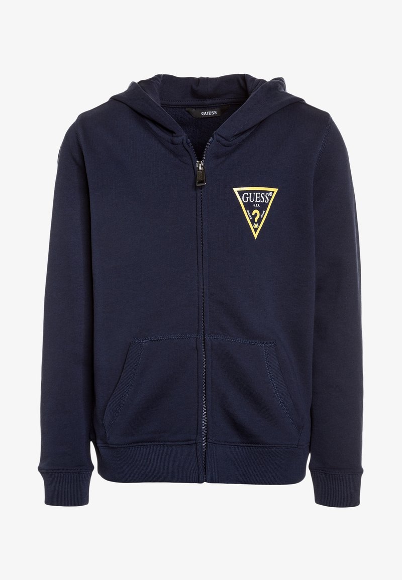 Hoodie zippé marine en mélange de coton. Il présente un logo triangulaire jaune "GUESS" sur la poitrine gauche et des poches kangourou. Texture douce.