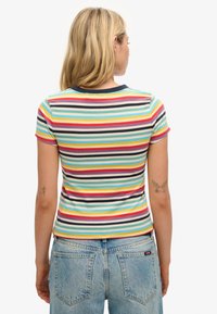 Stribet t-shirt med flerfarvede lodrette striber, korte ærmer og en marineblå krave. Båret med lyseblå højtaljede jeans.