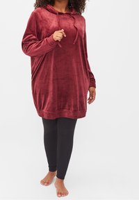 Karmesinrotes Velours-Hoodie-Kleid mit langen Ärmeln, gerippten Bündchen und Saum; getragen über schwarzen Leggings, mit einem lockeren Schnitt und weicher Textur.