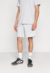 Ανοιχτό γκρι κοντομάνικη μπλούζα και ταιριαστά σορτς από μαλακό ύφασμα. Μαύρα αθλητικά παπούτσια με λευκές λεπτομέρειες και γκρι κάλτσες με λογότυπο.