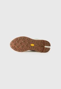 Brown rubber outsole with a textured pattern, featuring a yellow Vibram logo. The upper part is visible, showing a sturdy design.