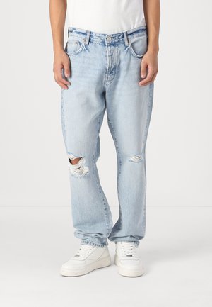 Jeans din denim de un albastru deschis, cu o croială lejeră, având două găuri deteriorate la genunchi, un design clasic cu cinci buzunare și o talie înaltă.