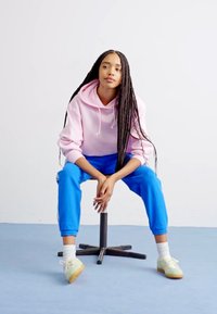 Ροζ φούτερ, μπλε παντελόνι φόρμας και πράσινα αθλητικά παπούτσια σε καθιστή φιγούρα. Λείες υφές με άνετη εφαρμογή. Απλός, μοντέρνος σχεδιασμός.