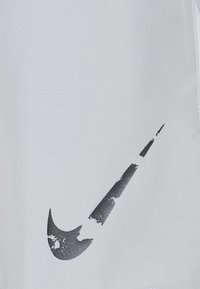 Logotipo de Nike en negro desgastado con partes despegadas y faltantes sobre un fondo de tela gris claro.