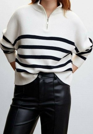 Weißer und marineblau gestreifter Strickpullover mit einem Viertel-Reißverschluss am Kragen; getragen über schwarzen Kunstlederhosen. Der Pullover hat eine lockere, lässige Passform.