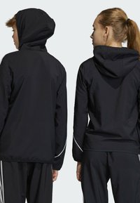 Zwarte sportjacks met capuchons, voorzien van witte accenten op de mouwen. Glad materiaal, normale pasvorm, gezien van achteren.