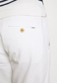 Weiße Leinenhose mit einer Gesäßtasche, die mit einem runden Holzknopf und einem "ESPRIT"-Label versehen ist. Der Stoff hat ein weiches, strukturiertes Aussehen.