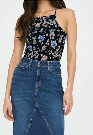 Kobieta w czarnej kwiecistej bluzce bez rękawów z cienkimi ramiączkami oraz w niebieskiej spódnicy jeansowej z wysokim stanem i przednim rozcięciem.