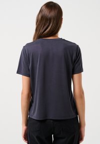 T-shirt grigio scuro a maniche corte con scollatura a girocollo e vestibilità rilassata, caratterizzato da una superficie liscia e dettagli di cucitura discreti sull'orlo.