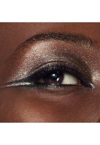 Close-up van een oog met een donkere eyeliner, glanzende zilveren oogschaduw en lange wimpers tegen een gladde bruine huid als achtergrond.