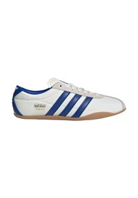 Vit sneaker med blå och grå detaljer, med tre randiga mönster, en gummisula och en gul logotyp som står "adidas TOKYO."