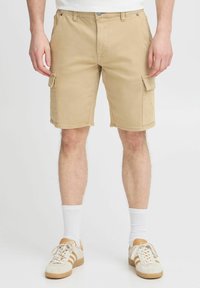 Pantalones cortos cargo beige con múltiples bolsillos, hechos de algodón, con un frente plano, trabillas para cinturón y una longitud casual por encima de la rodilla.