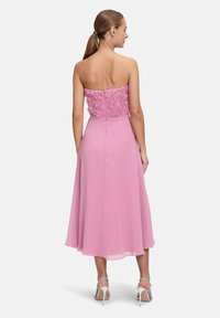 Robe rose sans bretelles avec un corsage floral texturé et une jupe fluide, dotée d'une taille ajustée et d'un détail de fermeture éclair à l'arrière.