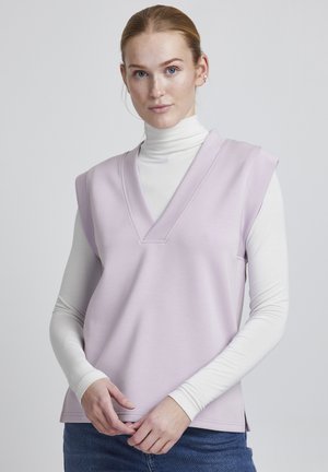 Helles lavendelfarbenes, ärmelloses Oberteil mit V-Ausschnitt, aus weichem Stoff, mit lockerer Passform und seitlichen Schlitzen. Über einem weißen Rollkragenpullover getragen.