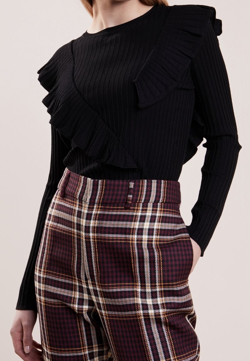 Haut noir à manches longues côtelé avec des détails à volants, associé à un pantalon taille haute à carreaux bordeaux et blanc.