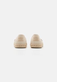 Paire de chaussures beige tissées à enfiler avec semelles en corde, vues de dos sur fond blanc uni.