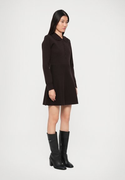 Robe longue marron à manches longues avec un col en feston et des détails de boutons, accompagnée de bottes en cuir noires montantes avec des talons carrés.