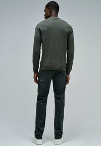 Šedá bavlněná mikina s ribbed manžetami a lemem, spárovaná s tmavými slim-fit džíny. Bílé tenisky dokončují outfit. Žádné viditelné vzory.