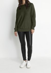 Mörkgrön, löst sittande tröja med ribbat avslut och muddar, i kombination med glänsande svarta leggings och vita sneakers. Slät textur genom hela plagget.