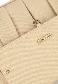 Bolsa de tela beige con textura acanalada, que presenta una etiqueta de hardware dorado y un lazo metálico. Detalle de costura en los bordes.