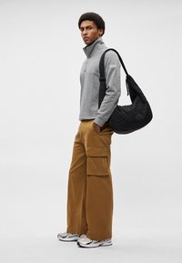 Γκρι φλις μπουφάν με φερμουάρ, μπεζ cargo παντελόνι με φαρδιά πόδια και τσέπες, μαύρη ραμμένη τσάντα ώμου και ασημένια αθλητικά παπούτσια.