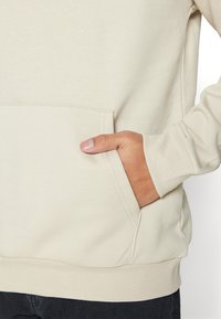 Lys beige sweatshirt med en kængurulomme. Den har en blød tekstur, ribbede manchetter og en afslappet pasform. Designet er uden synlige logoer.