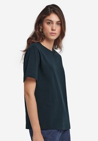 Mörkgrön bomullströja, avslappnad passform, korta ärmar, rund halsringning, slät textur, inga synliga mönster eller detaljer.