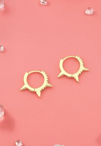 Goldene Creolenohrringe mit einem stacheligen Design und kleinen klaren Edelsteinen entlang einer Kante. Glatte Oberfläche, kreisförmige Form.