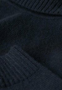 Tejido de suéter negro de punto, que muestra un fino ribete y una textura suave, con una sensación blanda. El tejido parece un poco estirado y acogedor.
