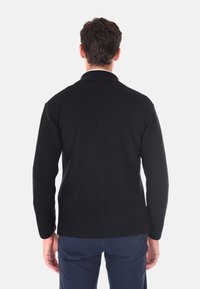 Giacca in maglia nera con un motivo testurizzato, colletto alzato e maniche lunghe. Il retro presenta una cucitura centrale e un orlo stondato.