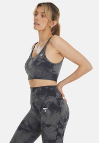 Zwart en grijs tie-dye sportbeha en hooggeknoopte legging met ribbelstructuur en logo-detail op het been. Rekbaar, lichaamsvolgend materiaal.