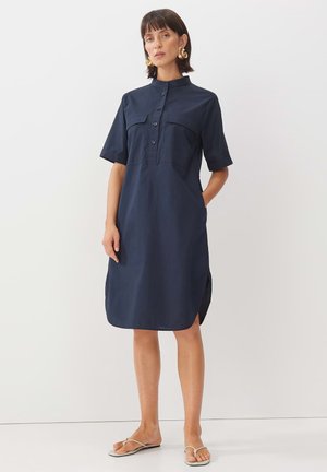 Navyblaues Hemdblusenkleid mit kurzen Ärmeln, Kragen, zwei Fronttaschen, Knopfleiste und seitlichen Schlitzen; aus leichtem Stoff gefertigt.