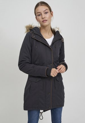 Parka gris foncé avec capuche en fausse fourrure, deux poches avant et taille à cordon. Présente des accents marron contrastants et des détails zippés.