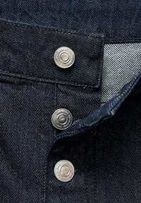 Mörk denimtyg med en subtil lyster, utrustad med silvermetallknappar i midjan och en texturerad innerfoder.