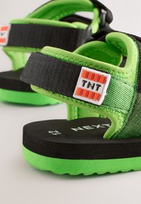 Groene en zwarte sandalen met verstelbare bandjes, gestructureerde stof, schuimzolen en een wit logo "THT" op het bandje.