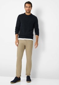 Granatowy sweter z dzianiny o prążkowanej fakturze, beżowe dopasowane spodnie, ciemne sneakersy. Model stoi na tle białym, z rękami luźno opuszczonymi.