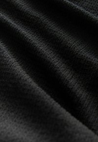 Svart texturerad tyg med ett subtilt mönster, som visar mjuka åsar och fåror, flödande i mjuka veck och skuggor.