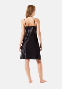 Vestido deslizante de satén negro con tirantes finos, de longitud a la rodilla, textura suave, forma en A y sutil brillo. Vista posterior que muestra detalles de diseño mínimos.