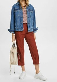 Denim jack, gestreepte rood-witte top, roestkleurige broek, witte sneakers en een beige tas met koorden. Casual outfit met contrasterende kleuren.