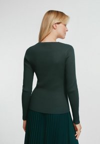 Ciemnozielony, długi rękaw, prążkowany sweter z okrągłym dekoltem, dopasowany fason i gładka tekstura, w połączeniu z plisowaną zieloną spódnicą.
