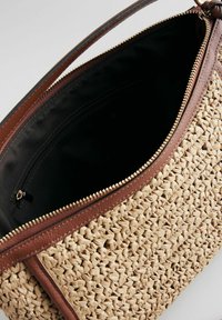 Sac en paille tissé avec des accents en cuir marron, doté d'une fermeture éclair dorée et d'un intérieur noir avec une poche zippée.